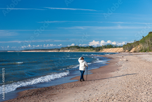 The girl walks along the sea on a sunny spring day.