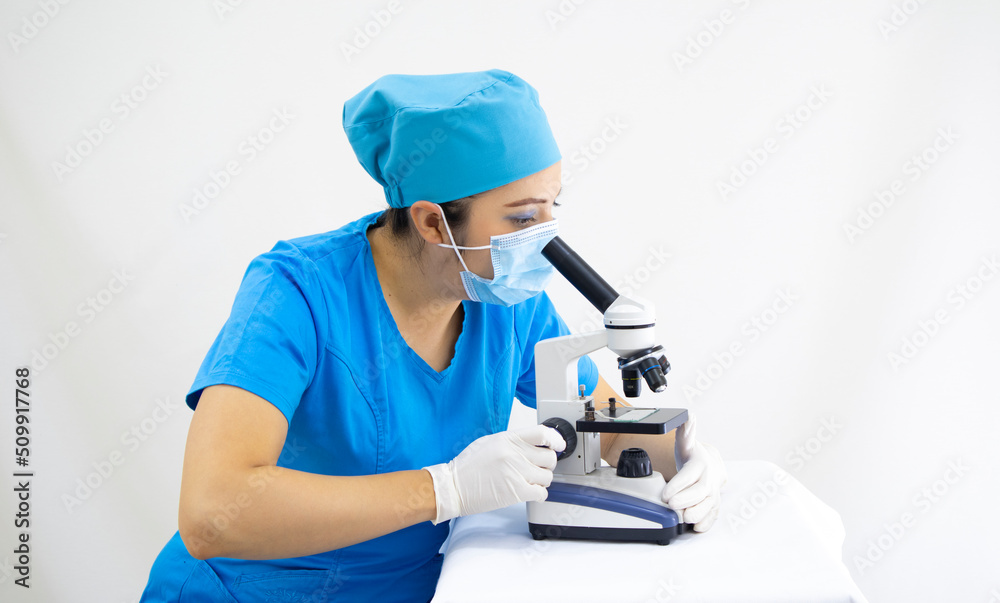 beautiful woman lab technician wearing uniform and blue surgical cap, surgical protection, analyzing samples with the microscope, on white background beautiful woman lab technician wearing uniform and blue surgical cap, surgical protection, analyzing samples with the microscope, on white background