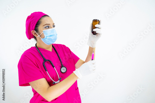 beautiful woman medical assistant wearing face mask, uniform and pink surgical cap, stethoscope and latex gloves, preparing injection on white background