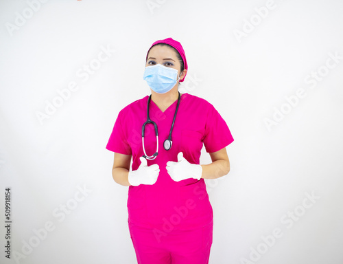 beautiful female medical assistant wearing face mask, pink uniform and pink surgical cap, latex gloves and stethoscope, on white background