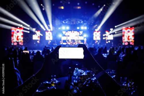 Smartphone in a hands on a music concert show, blank white screen mockup.
