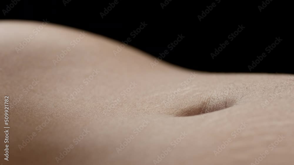 Macro shot of belly of young African American slim female model moving on black background | Skin texture shot for body care concept Macro shot of belly of young African American slim female model moving on black background | Skin texture shot for body care concept
