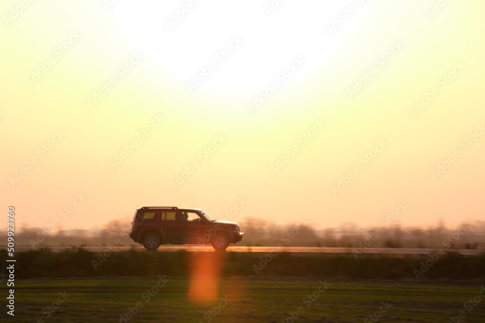 Fototapeta premium SUV car driving fast on intercity road at sunset. Highway traffic in evening