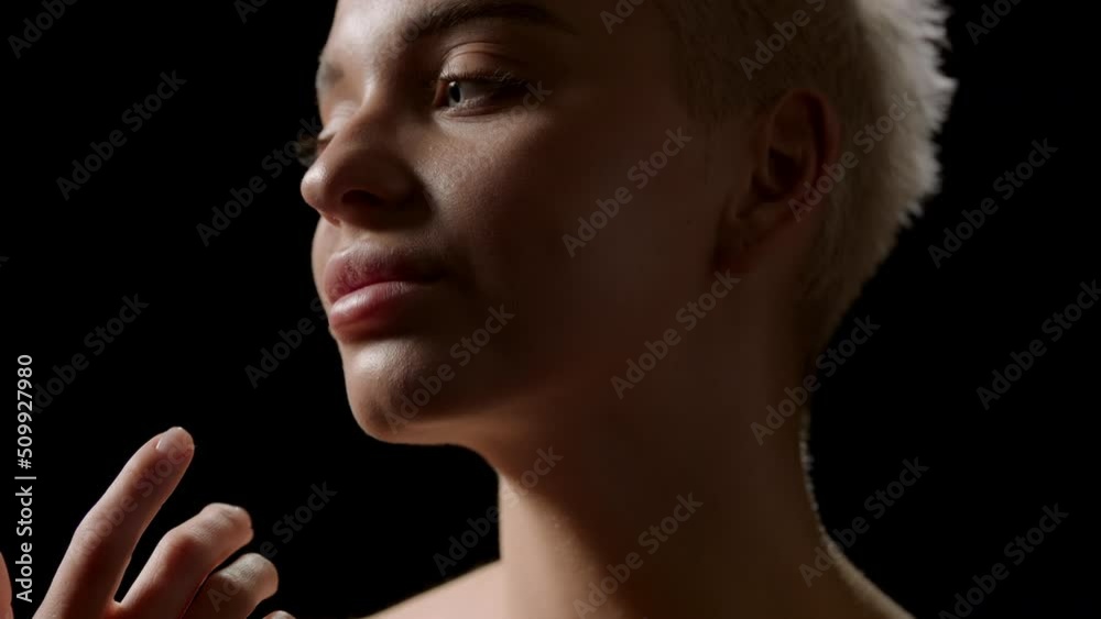 Close-up beauty portrait of beautiful young slim blond Caucasian woman strokes her jawline on black background | Sagging jowls removal concept Close-up beauty portrait of beautiful young slim blond Caucasian woman strokes her jawline on black background | Sagging jowls removal concept
