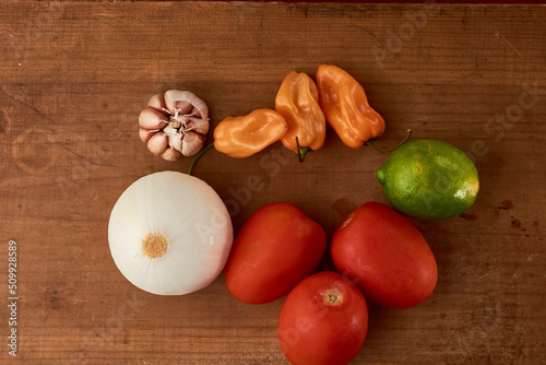 Yellow habanero chili, red tomatoes and white onion all placed on a wooden base