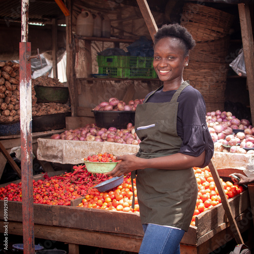 A beautiful and happy African Nigerian female trader, seller, business woman or shop owner preparing to sell goods to her customers in a market