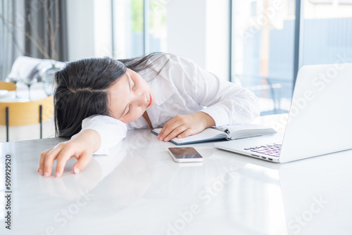 Young asian tired business woman with long hair working at laptop in bright home office