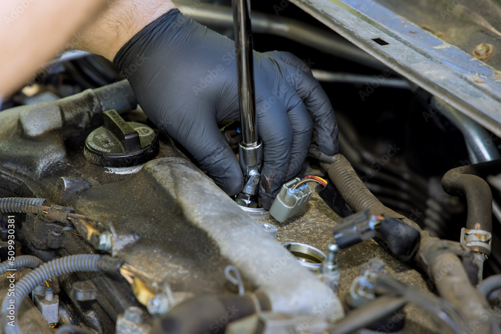 Auto mechanic makes repairs in garage service with unscrews old car candles are replaced for new spark plug Auto mechanic makes repairs in garage service with unscrews old car candles are replaced for new spark plug