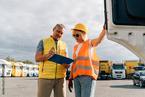 Mature woman and man at cargo warehouse, truck drivers delivery inspection 