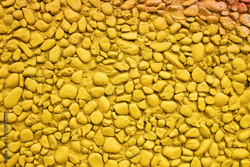 Wall of small stones painted yellow. Bright textured background. Copy space. 