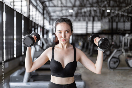 exercise concept The healthy woman in dark sport clothes tying her hair up and working out with weightlifting, carrying two black dumbbells up