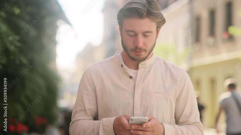 Close up of attractive man hold smartphone, watching social media standing on a city street. Smiling young guy texting on her phone. Close up of attractive man hold smartphone, watching social media standing on a city street. Smiling young guy texting on her phone.