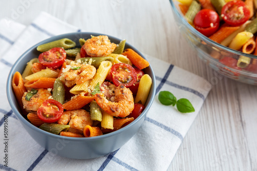 Homemade Tri-Color Penne Salad with Shrimp, Tomato and Basil Bread Crumbs in a Bowl on a white wooden background, side view.