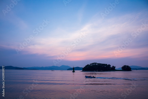 There is an island on the sea at sunset and people who enjoy riding boats