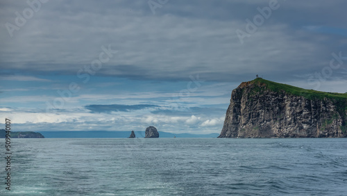 Islands in the Pacific Ocean. Steep rocky slopes, green vegetation on the hills. Ripples on the blue water. Clouds in the sky. Kamchatka. Avacha Bay photo