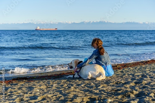 Girl sitting on the beach with her white dog - Esquimalt Lagoon, greater Victoria, British Columbia, Canada  photo