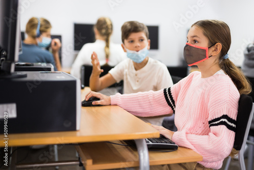 Young boy and girl in face masks using computers during lesson in computer class.