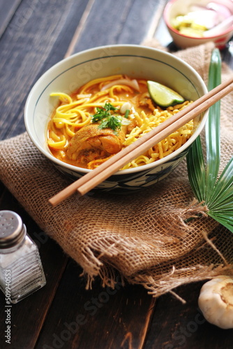 Khao Soi Recipe,Khao Soi,Khao Soi Kai, Thai Noodles Khao Soi, Chicken Curry with seasoning served on black wooden table with decorative leaves, vertical photo.