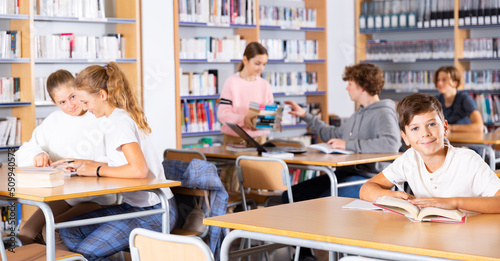 Ten-year-old schoolboy, preparing for lessons in the school library, takes notes in an exercise book of the necessary ..material from the textbook