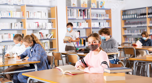 Group of intelligent girls and boys in face masks preparing for exams in library. Teenager girl looking in camera.