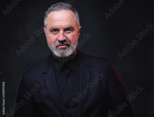 Portrait of handsome elderly dressed in black formal clothes with stylish hairstyle against dark background.