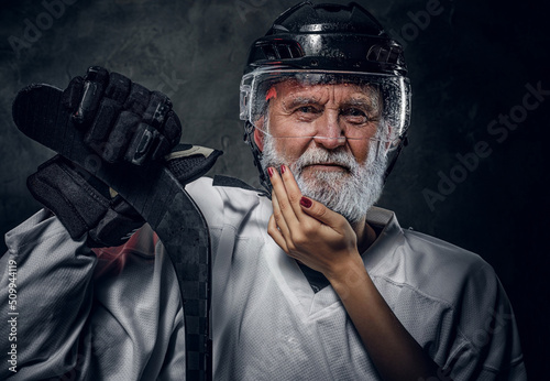 Photography Shot of serious old man hockey player with hockey stick being touched by woman against dark background