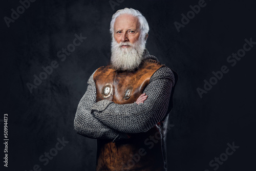 Shot of self confident elderly warrior dressed in antique armor with crossed arms against dark background. photo