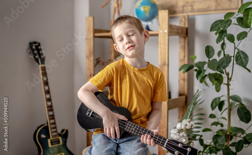 Cute cheerful boy is playing ukulele guitar in the music room. Joyful learning to play musical instruments photo