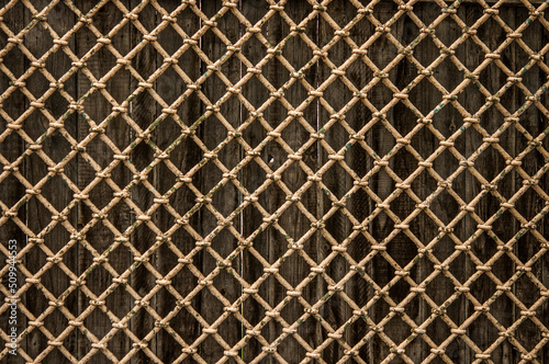 Old gray wooden wall behind a rusty metal rhombic grate. Background, texture.
