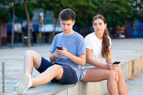 A coulpe of teenagers with smartphones is sitting on the step