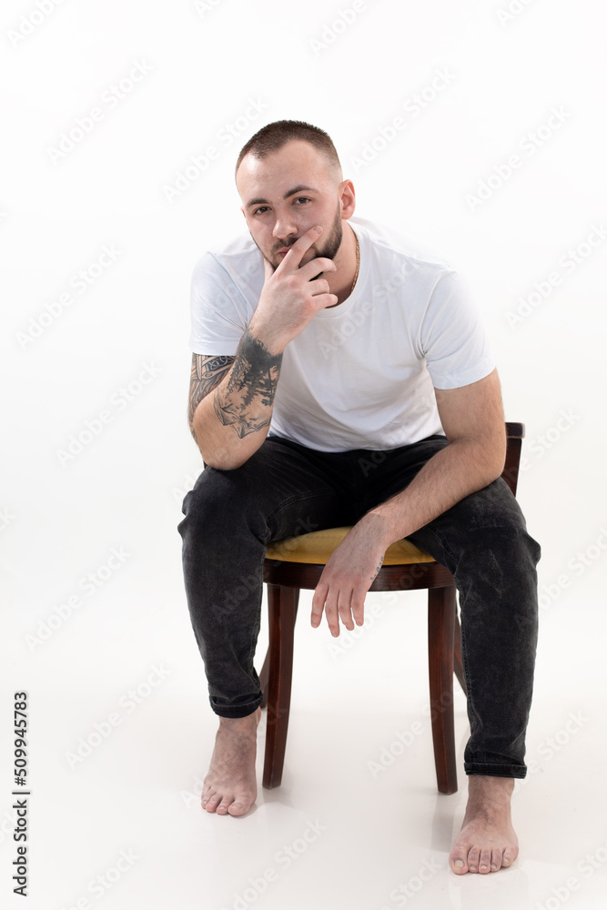 Portrait of tattooed handsome brutal brunet thinking bearded barefoot 40s man on chair. Modern, trendy successful male Portrait of tattooed handsome brutal brunet thinking bearded barefoot 40s man on chair. Modern, trendy successful male