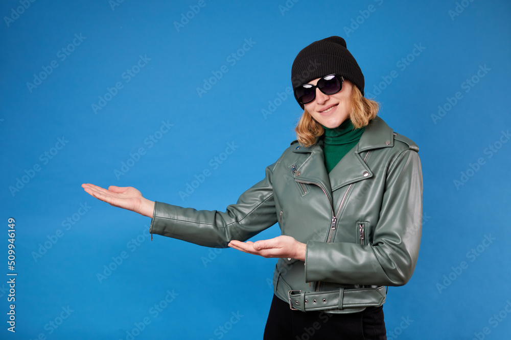 Look at commercial proposal. Cheerful woman pointing at copy space on her palm, empty place for idea presentation, product advertising. Indoor studio shot isolated on blue background
