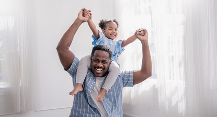 Happy black African American father daughter playing at home living room. Afro man carry piggyback little toddler girl. Cheerful family bonding together father’s day concept banner with copy space