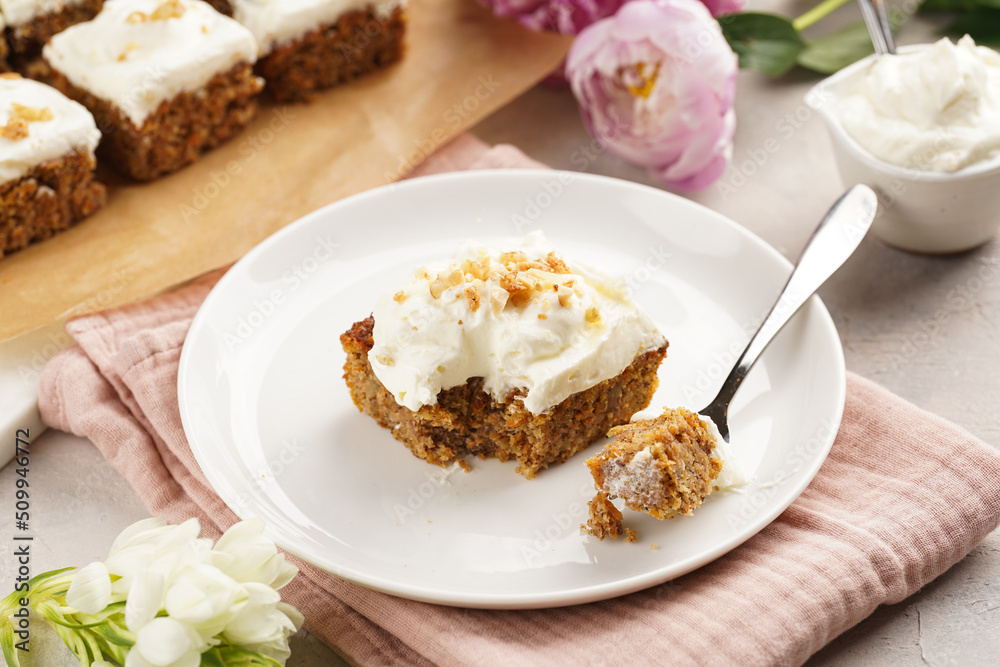 Homemade pastry carrot-walnut cake with grounded almonds and hazelnuts and white cream cheese top layer on white plate on pink napkin