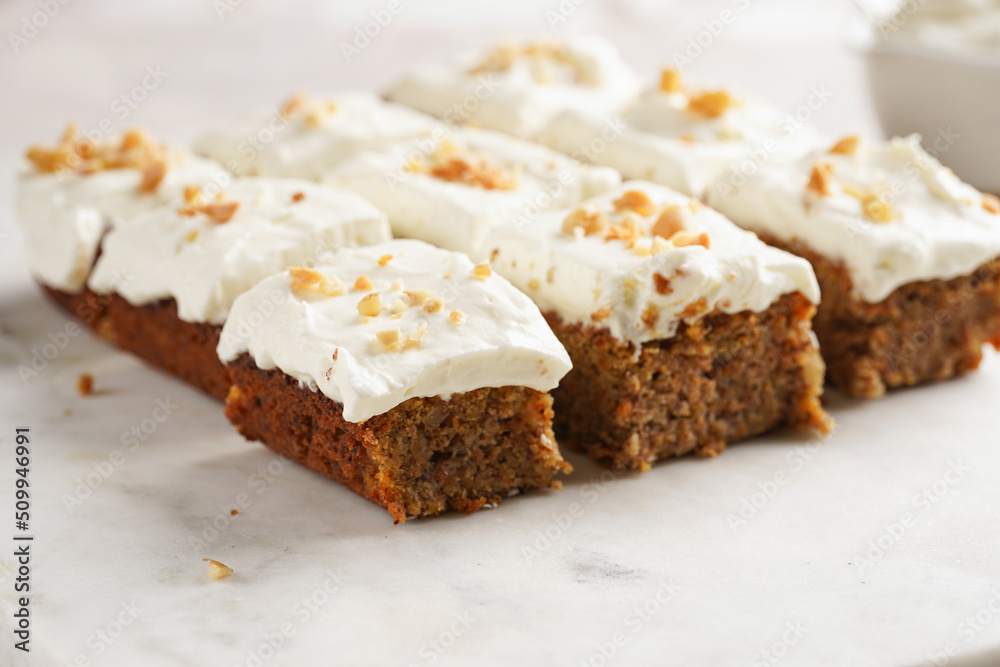 Homemade pastry carrot-walnut cake with grounded almonds and hazelnuts and white cream cheese top layer on marble board