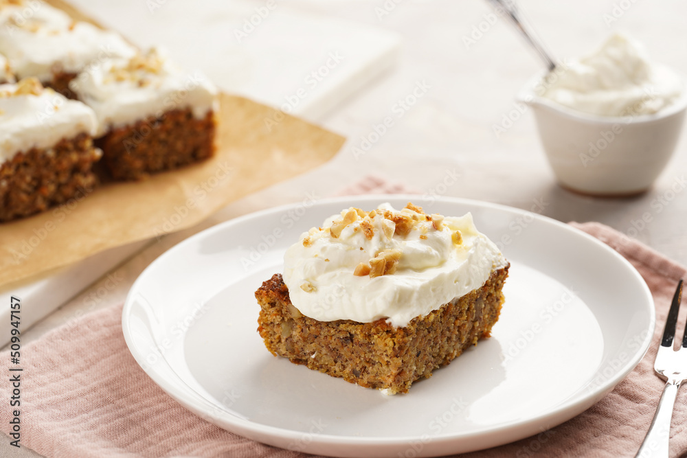 Homemade pastry carrot-walnut cake with grounded almonds and hazelnuts and white cream cheese top layer on white plate on pink napkin Homemade pastry carrot-walnut cake with grounded almonds and hazelnuts and white cream cheese top layer on white plate on pink napkin