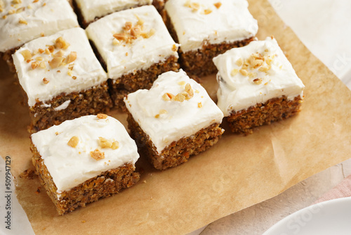 Homemade pastry carrot-walnut cake with grounded almonds and hazelnuts and white cream cheese top layer: several cut pieces on parchment paper