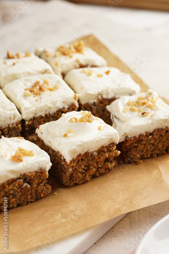 Homemade pastry carrot-walnut cake with grounded almonds and hazelnuts and white cream cheese top layer: several cut pieces on parchment paper