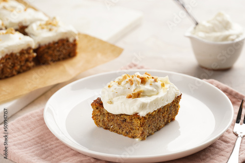 Homemade pastry carrot-walnut cake with grounded almonds and hazelnuts and white cream cheese top layer on white plate on pink napkin