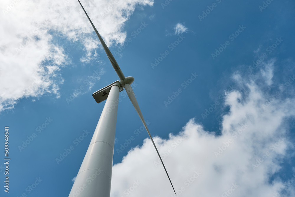 Wind turbine against saturated blue sky with white clouds. Low angle view of white wind turbine. Concept of clean energy Wind turbine against saturated blue sky with white clouds. Low angle view of white wind turbine. Concept of clean energy