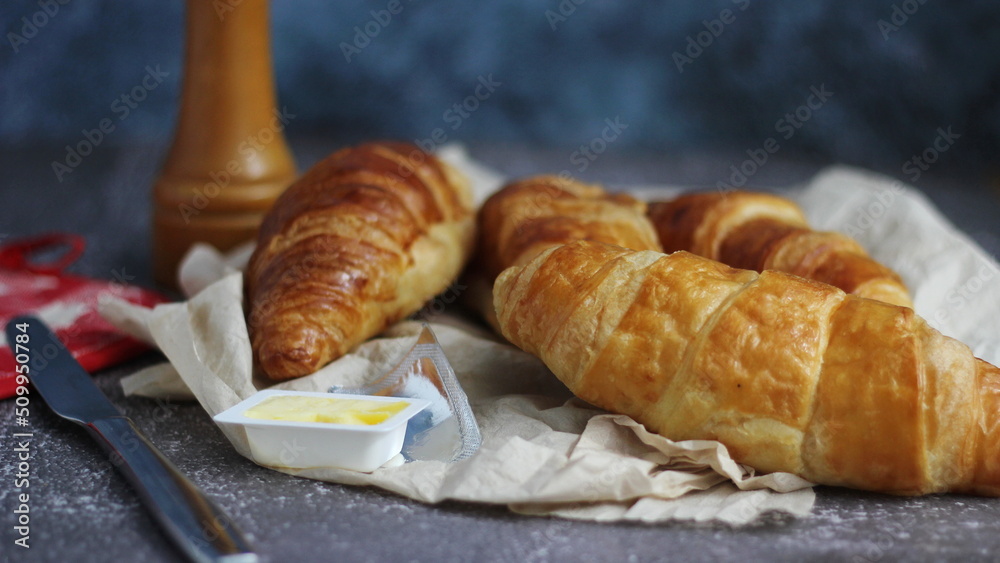 A pile of delicious fresh croissants served with butter. On a gray table with a blue background. A pile of delicious fresh croissants served with butter. On a gray table with a blue background.