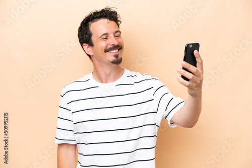 Young caucasian man isolated on beige background making a selfie © luismolinero