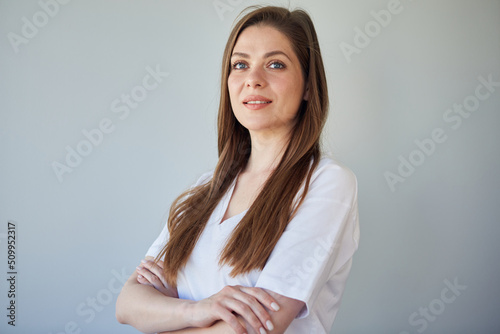 Smiling woman with long hair wearing white shirt standing with crossed arms and looks away. isolated portrait.