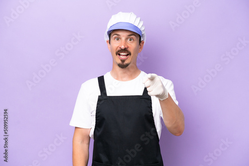 Fishmonger man wearing an apron isolated on purple background surprised and pointing front