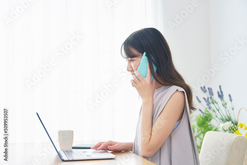 リビングでノートパソコンを見て電話する女性
