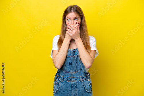 Young caucasian woman isolated on yellow background covering mouth and looking to the side