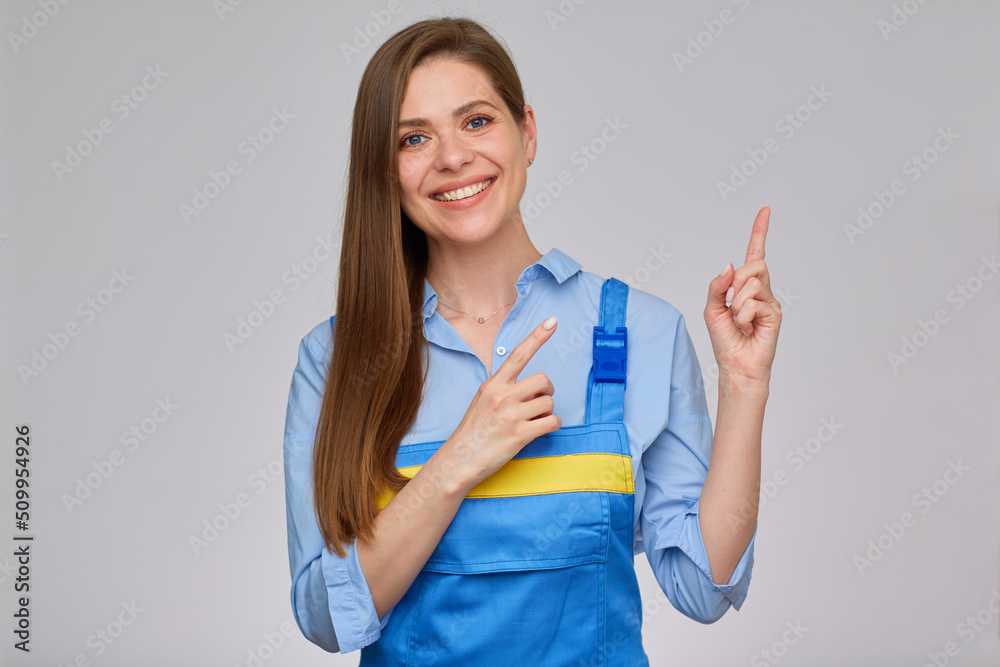 Smiling woman in blue overalls pointing her finger up to empty space. isolated portrait of happy worker girl with long hair. Smiling woman in blue overalls pointing her finger up to empty space. isolated portrait of happy worker girl with long hair.