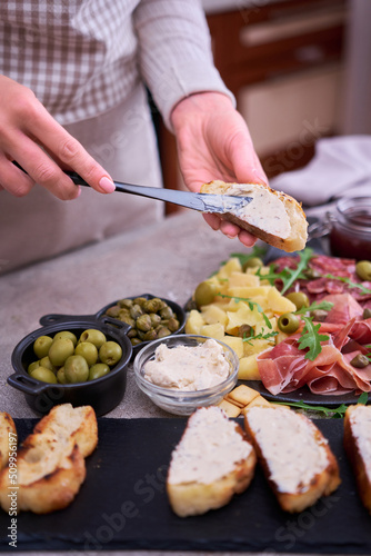 Woman spreading butter on grilled piece of baguette with Italian antipasto meat platter on background