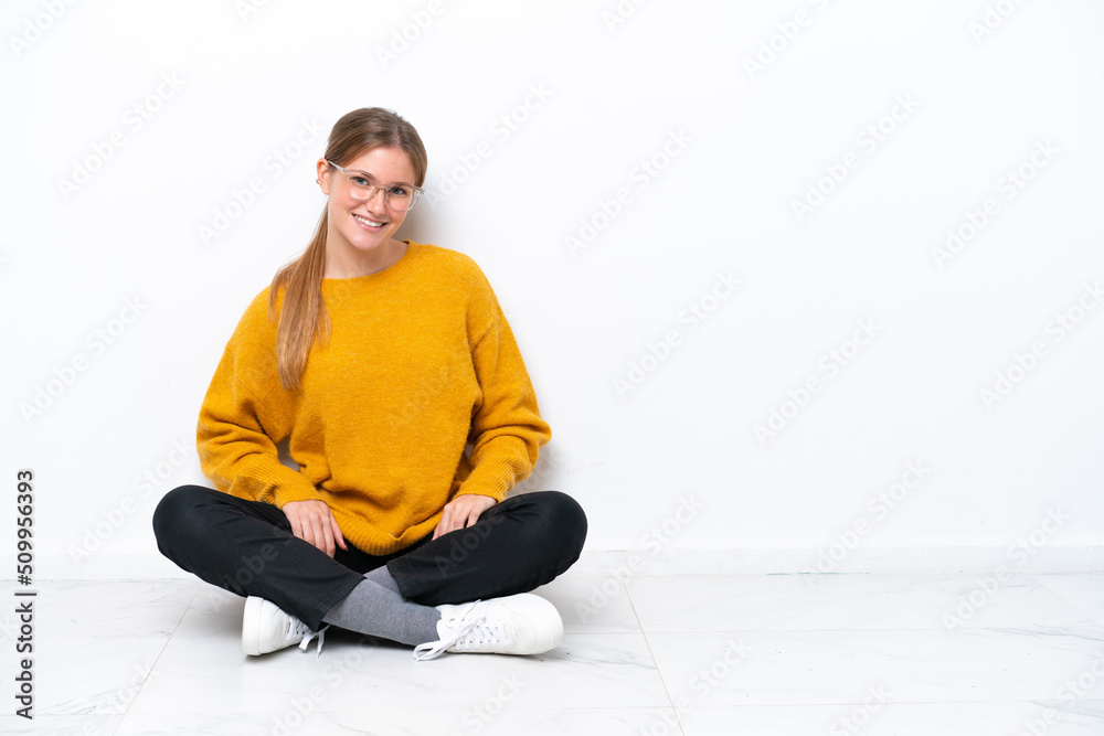 Young caucasian woman sitting on the floor isolated on white background laughing