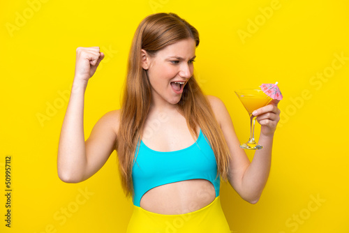 Young caucasian woman holding a cocktail isolated on yellow background celebrating a victory